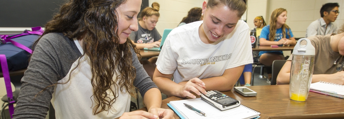 students at a desk working together using a calculator